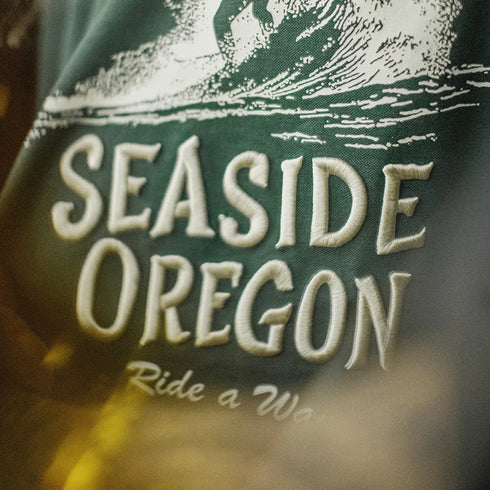 Text 'Seaside Oregon Ride a Wave' on a green background with wave design.